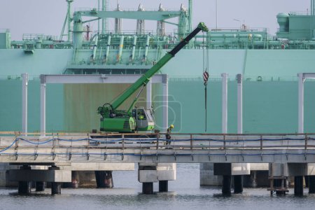 Foto de SEA PORT - Trabajadores y maquinaria de construcción en una terminal de gas con un petrolero de GNL en segundo plano - Imagen libre de derechos