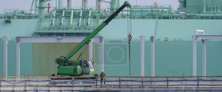 Foto de SEA PORT - Trabajadores y maquinaria de construcción en una terminal de gas con un petrolero de GNL en segundo plano - Imagen libre de derechos