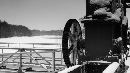 Foto de CONSTRUCCIÓN HIDROTÉCNICA - Rueda de engranaje y otros elementos de un vertedero en un lago en el paisaje de nieve e invierno - Imagen libre de derechos