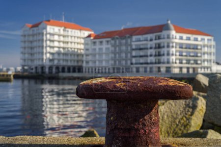A CITY BY THE SEA - Old rusty bollard on the port quay and a holiday resort in the background