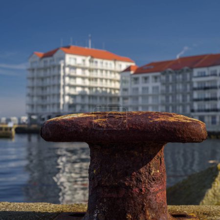Eine Stadt am Meer - Alter rostiger Poller am Hafenkai und eine Ferienanlage im Hintergrund