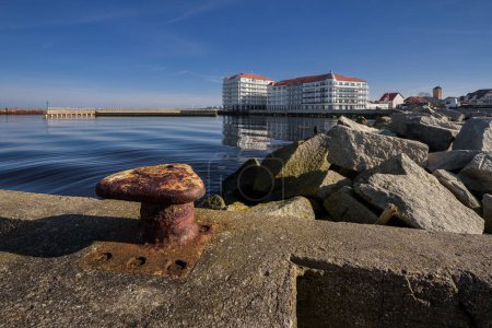 Eine Stadt am Meer - Alter rostiger Poller am Hafenkai und eine Ferienanlage im Hintergrund