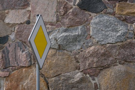 PRIORITY ROAD - Verkehrszeichen vor dem Hintergrund einer Steinmauer