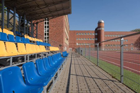 SPORTS FACILITIES - Grandstands for spectators at an athletics stadium and shool building on background
