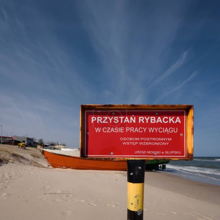Foto de PESCA HARBOR - Un cartel con una advertencia "Puerto pesquero - No hay acceso a los forasteros cuando el cabrestante está funcionando - Oficina Marítima en Slupsk" en el fondo de los barcos de pesca - Imagen libre de derechos