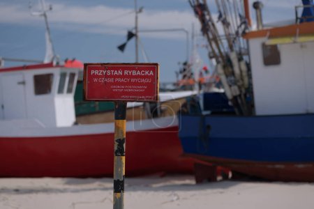 FISHING HARBOR - A sign with a warning "Fishing harbor - No access to outsiders when the winch is working - Maritime Office in Slupsk" against the background of fishing boats