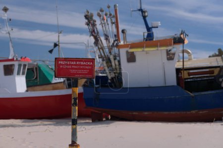 Foto de PESCA HARBOR - Un cartel con una advertencia "Puerto pesquero - No hay acceso a los forasteros cuando el cabrestante está funcionando - Oficina Marítima en Slupsk" en el fondo de los barcos de pesca - Imagen libre de derechos