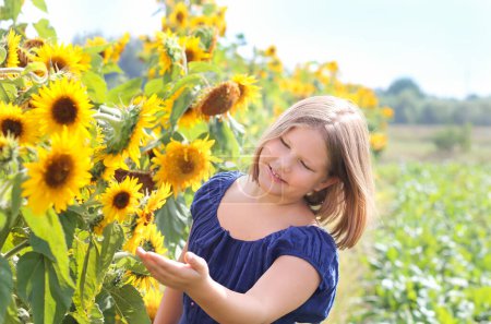 Schöne ukrainische Mädchen trägt blaues Kleid lächelnd zur Sonnenblume auf dem Sonnenblumenfeld. Ukraine Unabhängigkeit, Verfassung, Einheit, Tag. Landwirtschaft, Ernte, Landwirtschaft Postkarte, Poster, Kalender