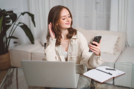 Foto de Young happy business woman, smiling pretty professional businesswoman worker looking at smartphone using cellphone mobile technology working at home or in office checking cell phone sitting at desk - Imagen libre de derechos