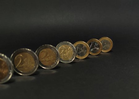 Blick auf Euro-Münzen auf dunklem Hintergrund, Fokus auf Rückmünzen, Ein-Euro- und Zwei-Euro-Münzen