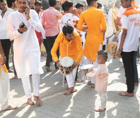 Foto de Jóvenes mostrando a un niño cómo tocar el damru en una procesión con motivo de Mahashivratri. Ubicación: Nashik, Maharashtra, India Fecha: 01 marzo 2022 - Imagen libre de derechos