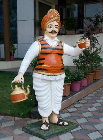 Téléchargez les photos : Statue représentant un vendeur de thé vêtu d'un costume coloré et d'un turban avec une bouilloire et levant une tasse de thé pour accueillir les invités s'arrêtant au restaurant. Lieu : Nashik, Maharashtra, Inde Date : 20 janvier 2024 - en image libre de droit