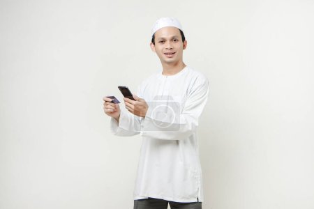 Foto de Guapo asiático hombre celebración de tarjeta de crédito y teléfono móvil en aislado fondo - Imagen libre de derechos