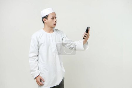Foto de Hombre musulmán sosteniendo el teléfono móvil y dar expresión de shock. Gente religiosa Islam concepto de estilo de vida. celebración Ramadán y ied Mubarak. sobre fondos aislados - Imagen libre de derechos