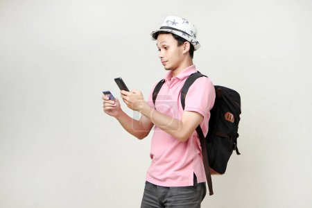 Foto de Hombre asiático mochilero celebración de teléfono móvil y tarjeta de crédito. nómada digital y concepto de viaje. sobre fondo aislado - Imagen libre de derechos