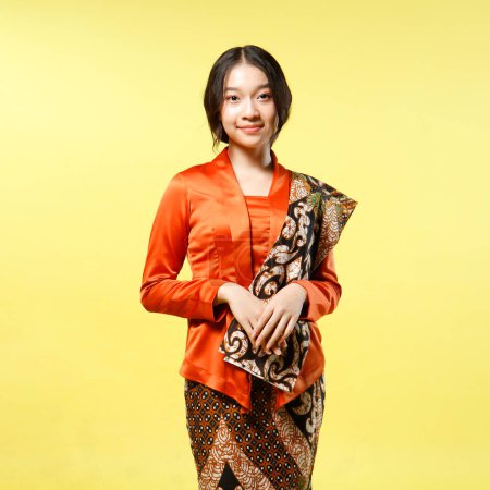 portrait of Beautiful young indonesian woman wearing modern kebaya kutu baru with batik shawl isolated on yellow background