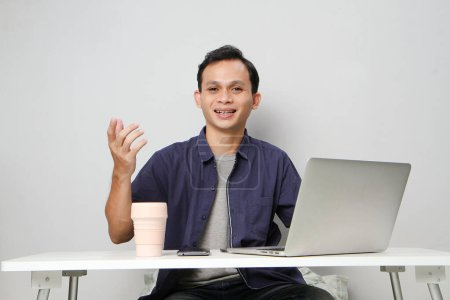 Foto de Feliz hombre asiático alegre en el lugar de trabajo mientras está sentado frente a la computadora portátil. sobre fondo aislado - Imagen libre de derechos