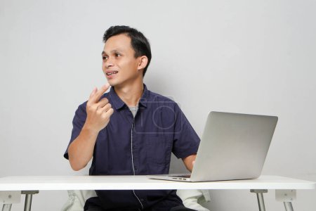 Foto de Alegre feliz asiático hombre en la videollamada en línea reunión señalando el dedo mientras está sentado delante de la computadora portátil. sobre fondo aislado - Imagen libre de derechos