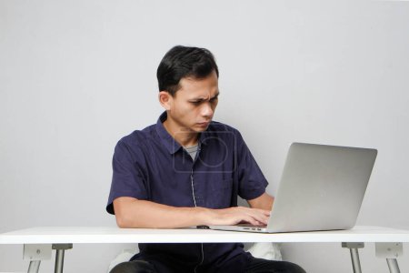 Foto de Concentrado cara de asiático hombre mientras sentado en frente de ordenador portátil. en un terreno de bakcground aislado - Imagen libre de derechos