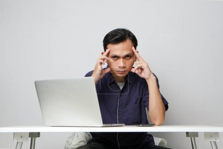 Foto de Concentrado cara de asiático hombre mientras sentado en frente de ordenador portátil. en un terreno de bakcground aislado - Imagen libre de derechos