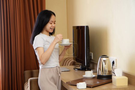 junge schöne asiatische Indonesien weibliche Füllung Becher mit heißem Wasser beim Brauen von Getränken. ziemlich elegante Dame im weißen T-Shirt gießen von Wasserkocher zu Tasse Tee kochen zu Hause Kochstelle am Morgen.