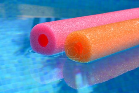 Photo for Summer vibes, colourful red and orange polyethylene swim noodles floating in blue tiled swimming pool - Royalty Free Image