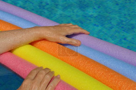 Photo for Rainbow coloured floating foam sticks and female hands, in swimming pool - Royalty Free Image