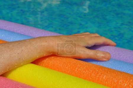 Photo for Rainbow coloured floating foam sticks and female hand, in swimming pool - Royalty Free Image