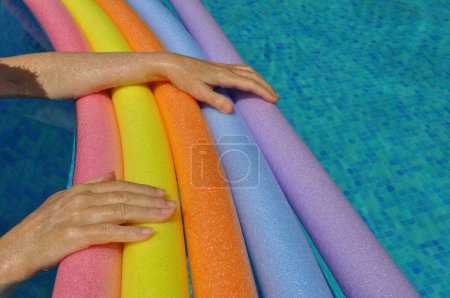Photo for Rainbow coloured floating foam sticks and female hands, in swimming pool - Royalty Free Image