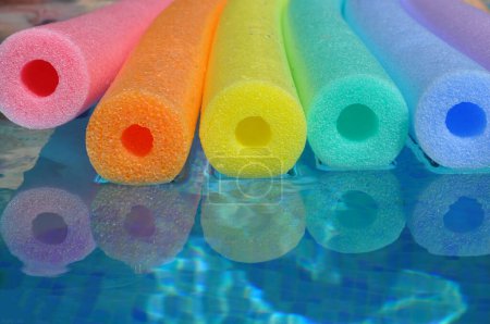 Photo for Rainbow colour polyethylene pool noodles floating in a blue tiled swimming pool, summer vibes - Royalty Free Image