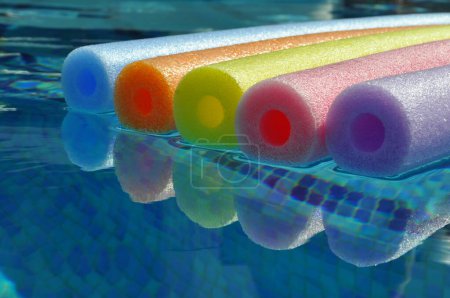 Photo for Rainbow coloured pool noodles floating in swimming pool, with reflection in water - Royalty Free Image