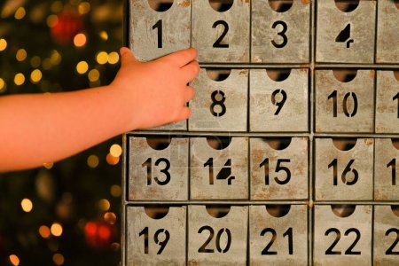 calendario de adviento en estilo vintage y mano de niños cerca del árbol de Navidad con juguetes guirnalda brillante sobre fondo borroso habitación. Tradiciones y símbolos de Navidad