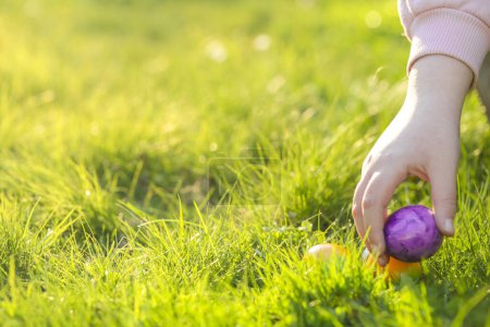 Caza de huevos de Pascua. Las manos de los niños recogen huevos en la hierba verde. Vacaciones de tradición cristiana y católica.Encontrar huevos de colores en la pradera.
