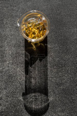 Foto de Aceite de hígado de bacalao. Omega-3.Fish cápsulas de aceite en frascos de laboratorio transparentes en un fondo de pizarra negro en la luz dura brillante con los ácidos grasos shadows.omega - Imagen libre de derechos