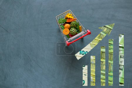 Steigende Lebensmittelpreise.Lebensmittelpreise in Europa.Dekoratives Gemüse und Obst und Euro-Scheine werfen Pfeile auf schwarzem Kreidetafelhintergrund.Lebensmittelkorbkosten in Europa.Lebensmittelpreise. Steigende Lebensmittelpreise 