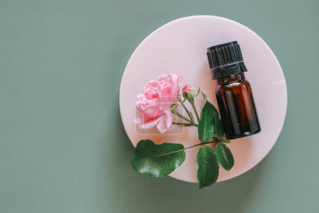 Rose water.cosmetics with rose extract.Rose oil in a bottle on a pink podium on a gray background. View from above .Aromatherapy and cosmetics.Organic natural rose oil.Organic bio cosmetics
