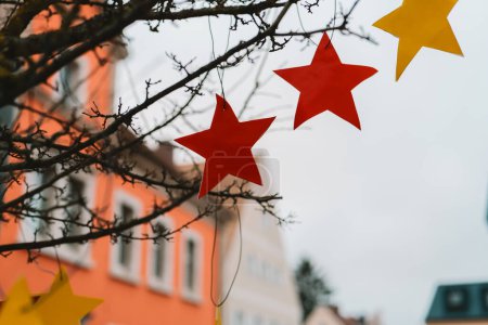 Christmas street decorations in European cities. Wooden red and yellow stars on tree branches. Holiday Wooden DIY Outdoor Decorations.Christmas time in Europe.
