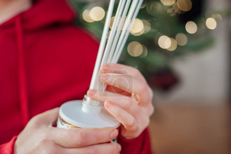 Fragrance diffusers with the scents of Christmas.incense sticks in a hand on a Christmas tree background.Diffuser with sticks with aroma on Christmas shining tree bokeh background.