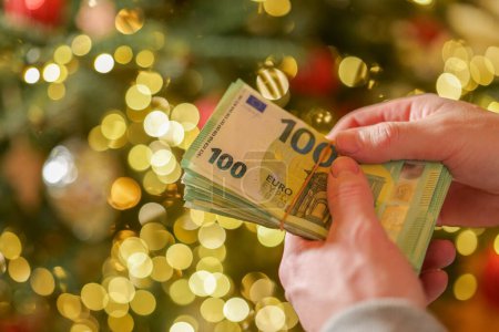 Christmas expenses and bills. euro money in hands on a Christmas shining spruce background.Spending on gifts and Christmas decor.Expenses during the winter holidays