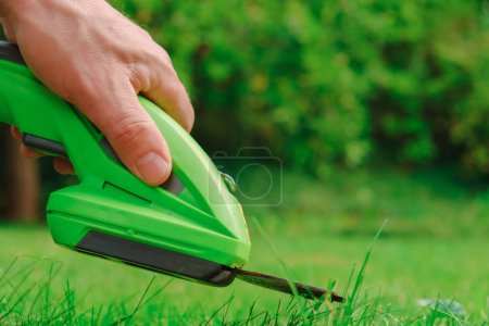 Rasentrimmer. Der elektrische Trimmer in der Hand eines Mannes schneidet in Großaufnahme das Gras. Prozess des Rasenmähens aus nächster Nähe. Gartengeräte und Werkzeuge.