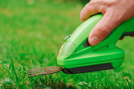 Rasentrimmer. Elektrischer Trimmer in der Hand eines Mannes schneidet das Gras. Prozess des Rasenmähens aus nächster Nähe. Gartengeräte und Werkzeuge.