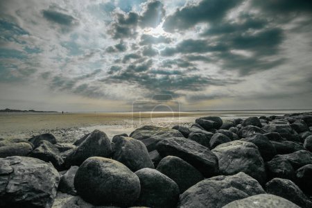 Stone boulders on the beach at low tide.Wadden Sea Coast.Stone groyne close-up on cloudy sky background.. Marine photo wallpaper.Nature of the North Sea coast. Frisian Islands of Germany. 