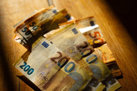  Billetes en euros sobre una mesa de madera en una franja de luz.Ingresos en los países europeos. Pagos en efectivo en los países de la UE.Ganancias y gastos en la zona euro. 