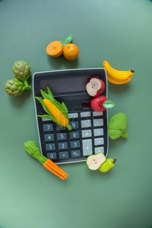 Gemüse- und Obstpreise. Lebensmittelkorbkosten. Lebensmittelkosten. Steigende Lebensmittelpreise. Taschenrechner und Gemüse Obst Deko auf grünem Hintergrund