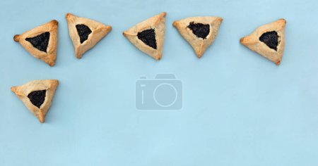 Téléchargez les photos : Biscuits triangulaires avec des graines de pavot (hamantasch ou aman oreilles) pour les vacances juives de la célébration de Pourim sur fond bleu avec espace pour le texte. Vue de dessus, plan plat - en image libre de droit