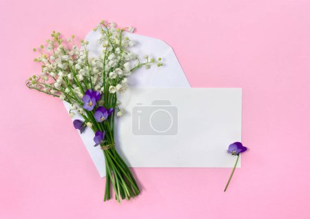Weiße Blüten Maiglöckchen (Convallaria, Maiglocken, Maiglöckchen), Briefumschlag mit Papierkartennotiz mit Platz für Text auf rosa Hintergrund. Draufsicht, flache Lage. Frühlingsdekoration