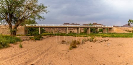 Photo for A view from the river bed towards the bridge over the Agab river at Oruhito in Namibia during the dry season - Royalty Free Image