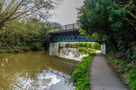 A view along the canal path towards an old railway bridge over the Grand Union Canal in Aylestone Meadows, Leicester, UK in Springtime