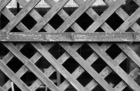 A weathered wooden trellis fence in monochrome 