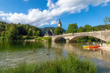 Foto de Lago Bohinj con barcos y turistas, Iglesia de San Juan Bautista con puente.Parque Nacional Triglav, Alpes Julianos, Eslovenia. - Imagen libre de derechos
